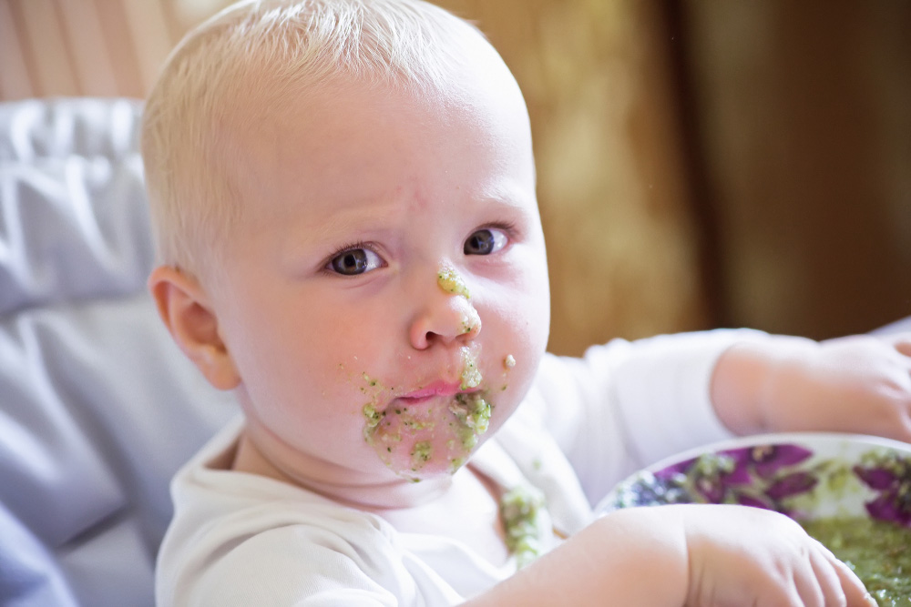A baby with food on its face and not looking happy