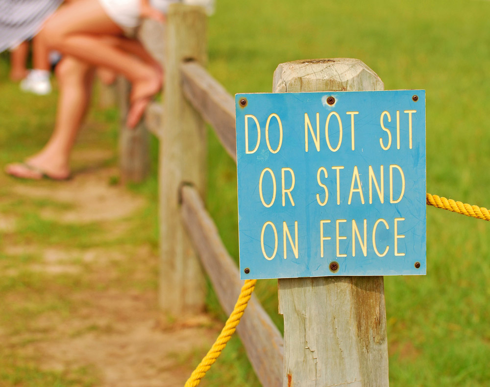 Sign saying do not sit or stand on the fence and people are sitting on it