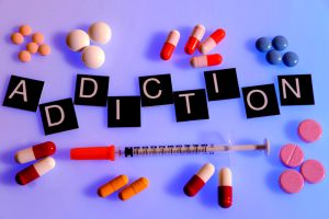 Pills a needle and the word addiction