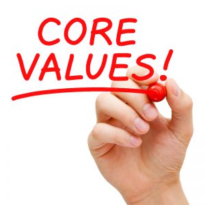 A hand holding a red pen that has written core values