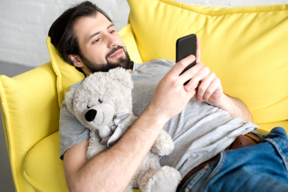 A man cuddling a teddy while looking at his phone