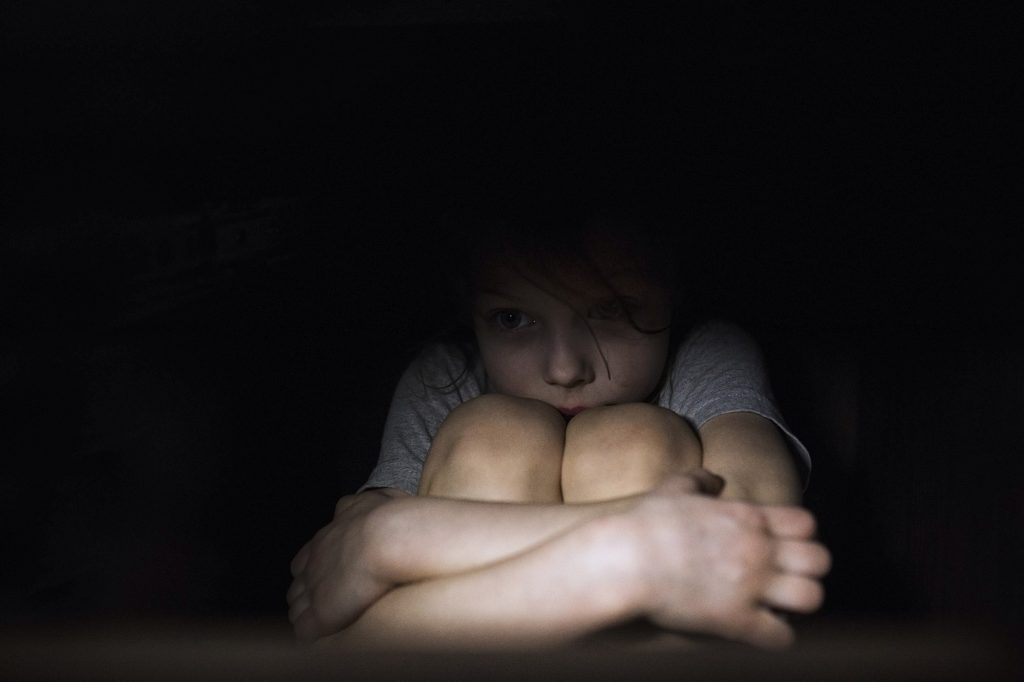 A worried child hunched up in the dark